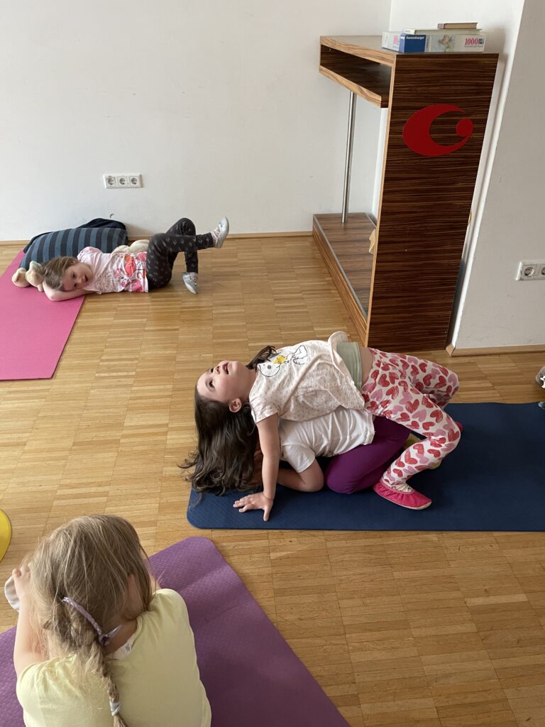 Kinder üben fröhlich Yoga-Posen unter Anleitung in einem Kinderyoga-Kurs.