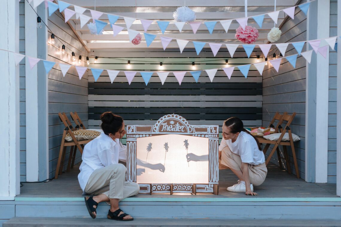 An outdoor puppet theater with women enjoying a creative afternoon in a decorated porch.