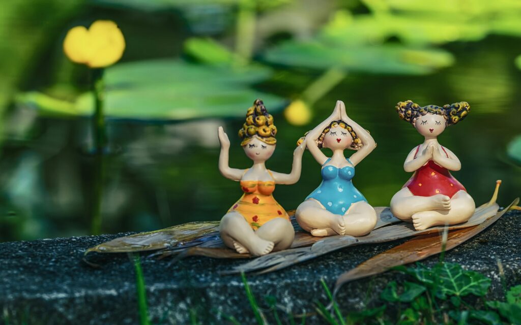 Three  figurines in yoga poses bring a playful charm by a peaceful pond.
